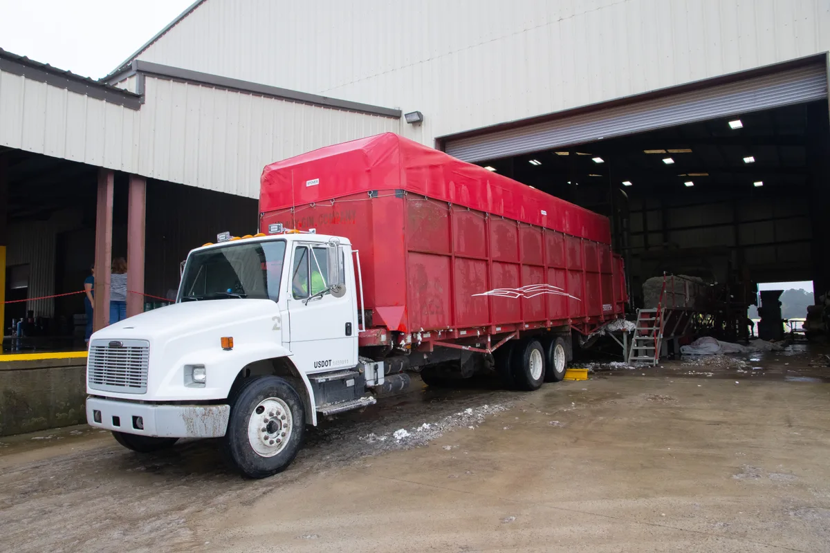 Stock photograph of a white truck with a red cargo body beside a warehouse